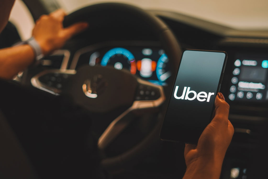 Are Rideshare Drivers on the Road to Financial Ruin? car driver looking at Uber app on smartphone