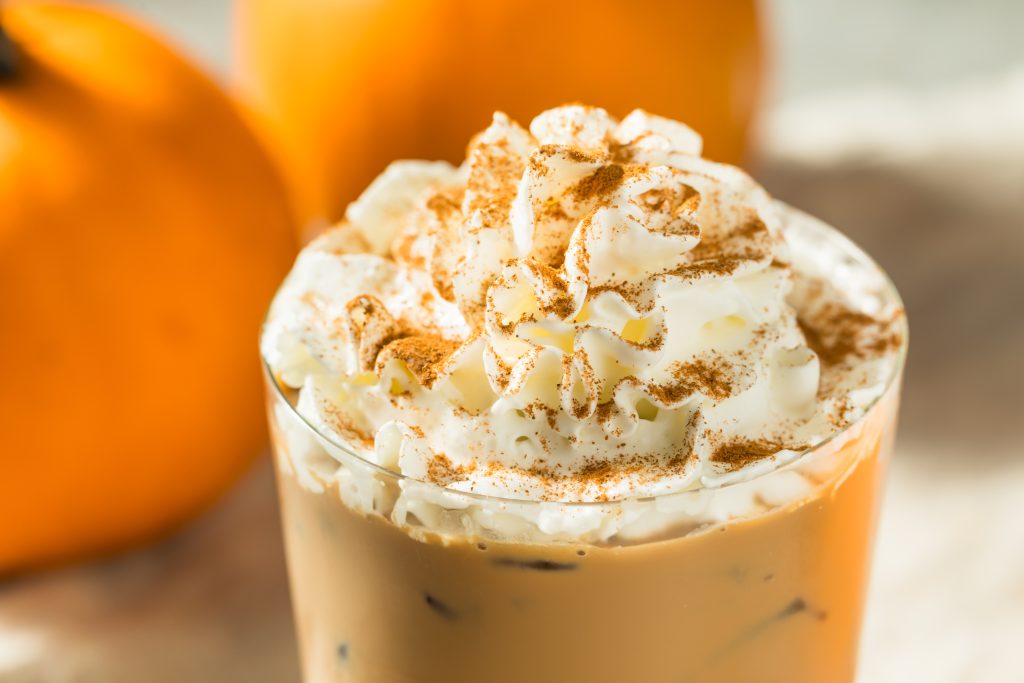Are Tariffs and the ‘Pumpkin Spice Tax’ Coming for Your Fall Coffee Budget? pumpkin spice latte in a glass next to real pumpkins