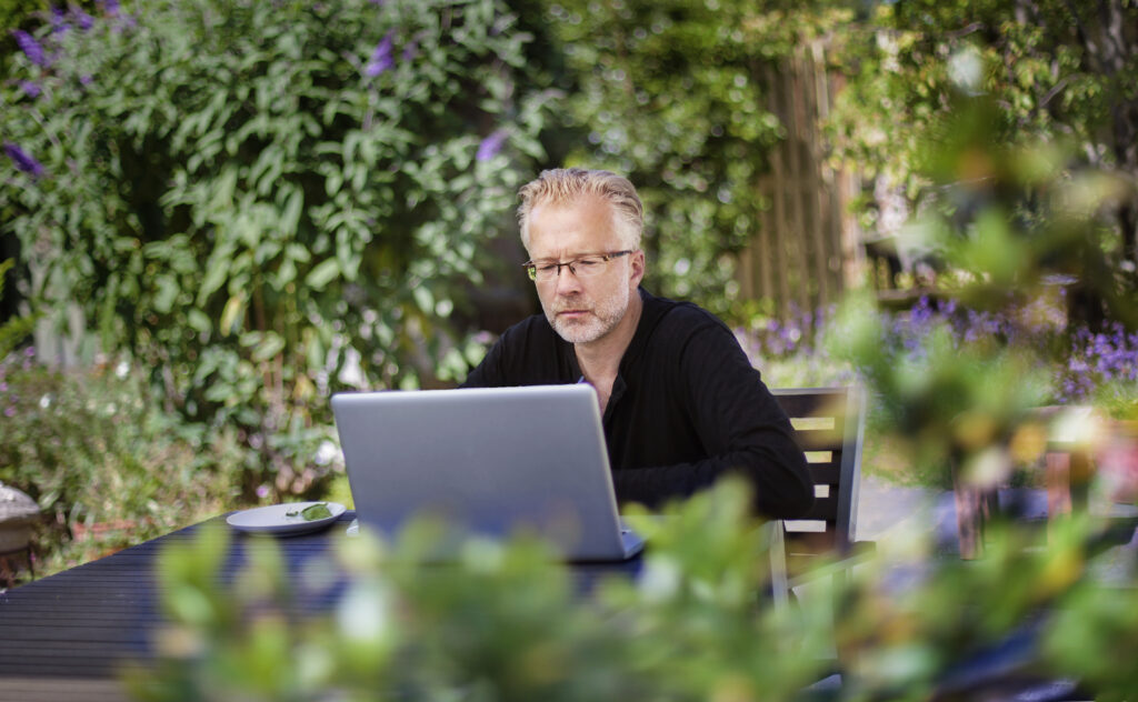 An older man concentrates on his laptop screen while checking 401(k) fees outdoors.