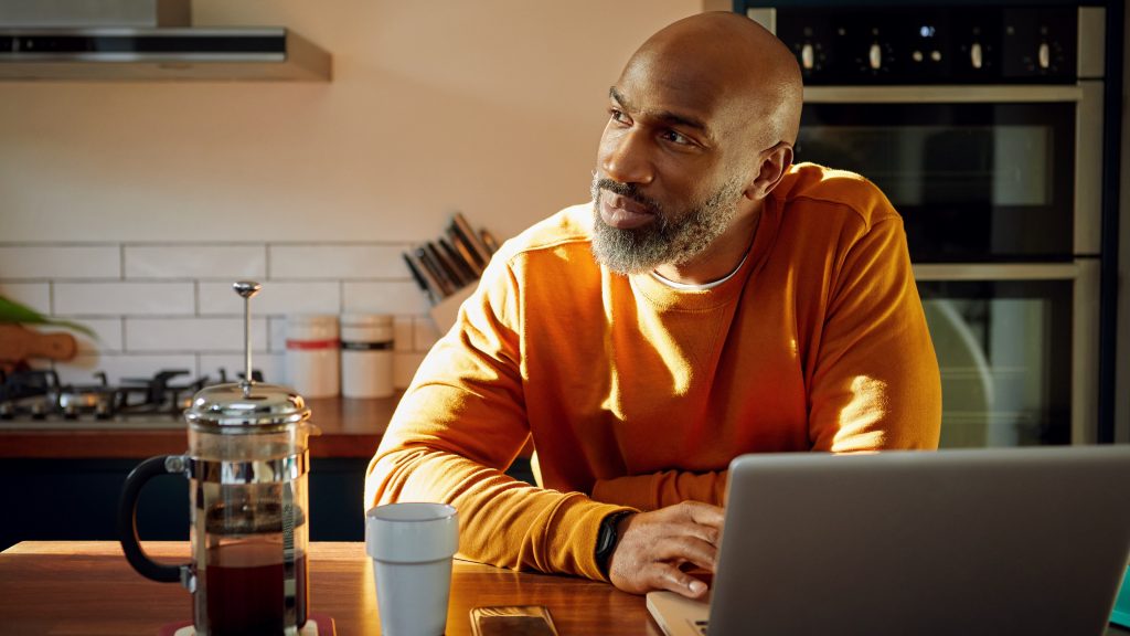 A man sitting at his kitchen island in front of his laptop looks like he's thinking.