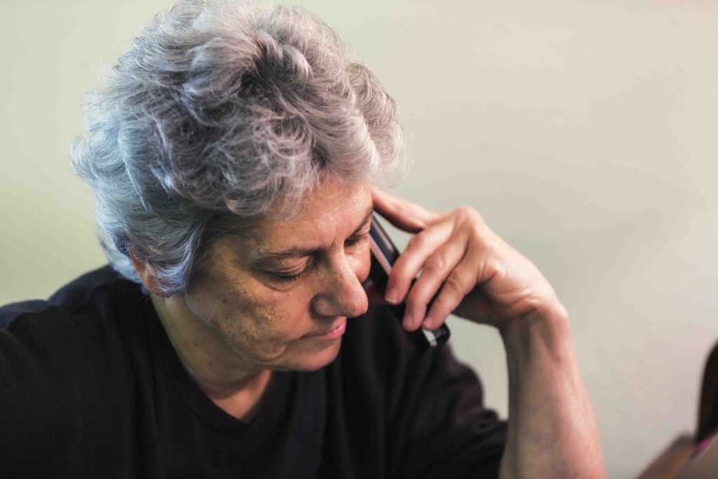 Need to Call Social Security? Be Ready to Hold An impatient older woman is waiting on hold on the telephone while sitting at her desk.