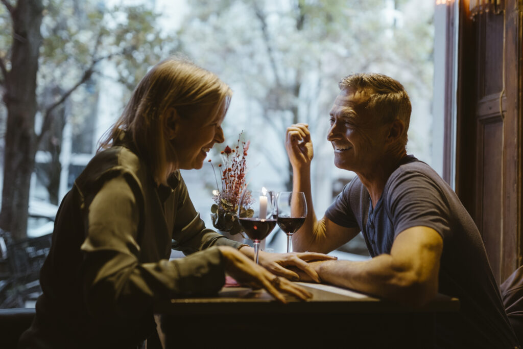 The Rule of Two Lives in Retirement An older couple laughs together in a restaurant. They are framed by a window and drinking wine.