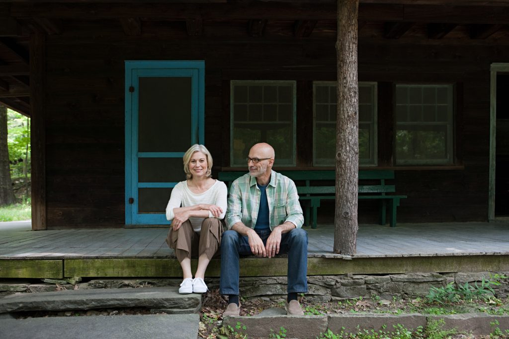 An older couple sits on the steps of a rustic vacation home.