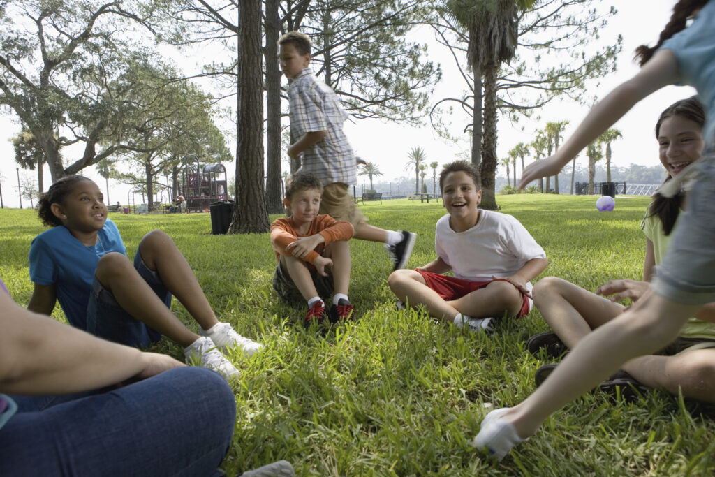 A group of children playing &quot;duck, duck goose&quot; outdoors.