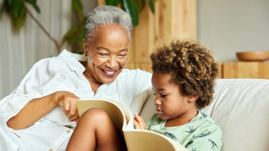 Don't Disinherit Your Grandchildren: Beneficiary Form Risks An older woman sits on the sofa with her grandson as they read a book together.