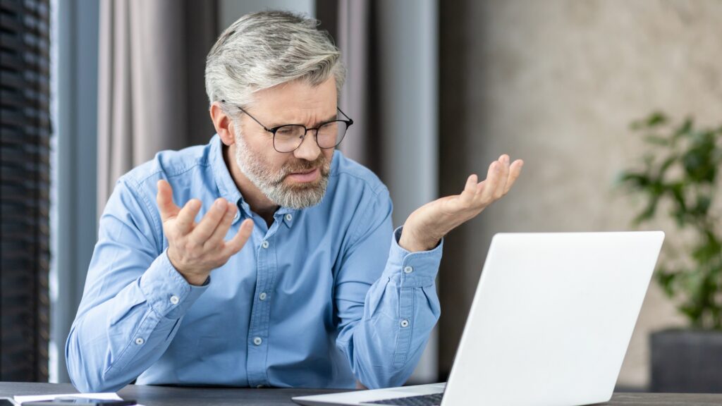Five Key Wake-Up Calls for Ambitious Business Owners An older businessman looks upset as he looks at his laptop at his desk.