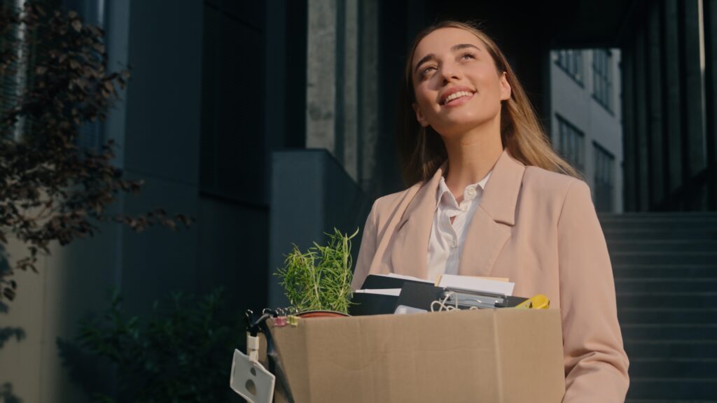From Job Loss to Free Agent: An Expert's Transition Playbook An optimistic-looking woman leaves an office building with a box full of personal items.