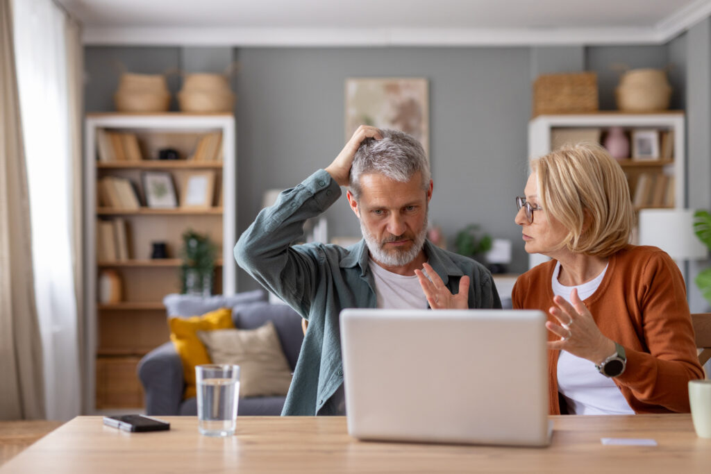 How to Avoid Money Market Account Fees and Protect Your Savings An older couple have an emotional discussion while looking at their laptop on the kitchen table.