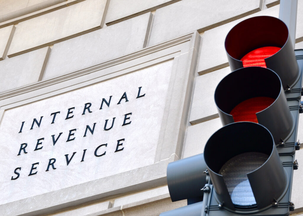 Shrinking IRS Staff and More Budget Cuts in 2025? What it Means for Taxpayers image of IRS sign with red traffic light in the foreground