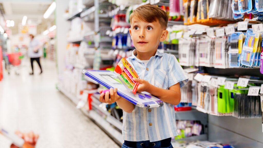 A young boy holds school supplies at a store.