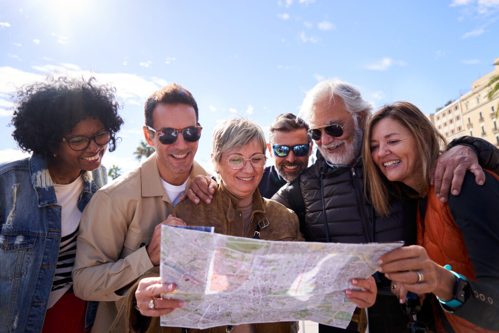 Solo vs Group Travel: What's Best for Retirees? Group of diverse mature people smiling looking at a travel map on the street of a touristic city.