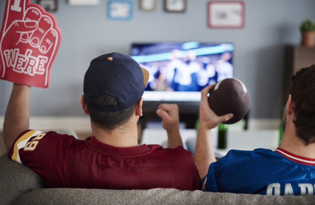 The Real Cost of Streaming Live Sports in 2025 Two people watching football on a couch