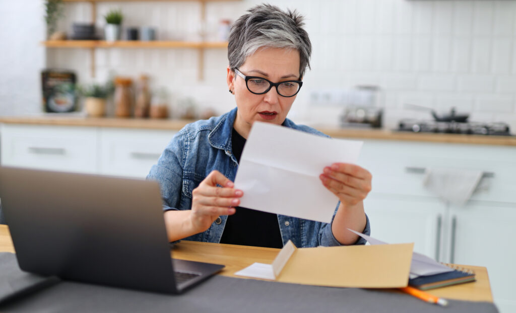 Shocked woman holding big Medicare bill at home.