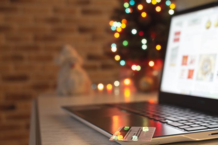 Christmas shopping online. Laptop and credit bank card on table at home on the background of a Christmas tree with blurred bokeh lights.